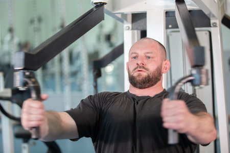 A man is working out with a machine that has a black handle. He is wearing a black shirt and has a...