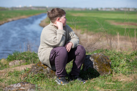 A chubby, plump teenage boy of twelve years old sits against the backdrop of nature and is sad.の写真素材