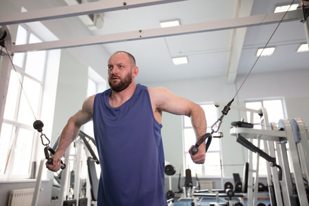 Male athlete bodybuilder exercising in the gym. Strength training on a cable machine.