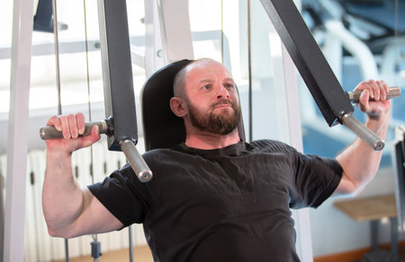 A man is working out at a gym, lifting weights and using a machine. He is focused and determined,...