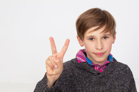 Portrait of a teenage boy with his fingers raised up on his hand. He is wearing a gray sweater and...