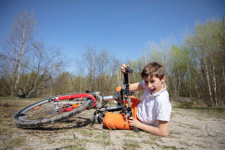 A boy is laying on the ground next to a broken bicycle. He is holding onto the handlebars and laughingの写真素材