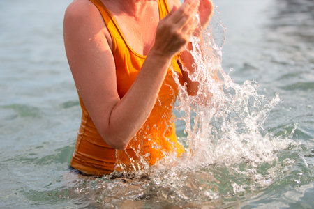 The hands of an unrecognizable woman in a yellow T-shirt splash sea water.の写真素材
