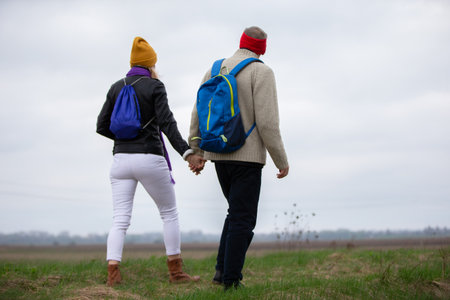 Active elderly Caucasian couple hiking with backpacks enjoying their adventure. They are walking along the field.の写真素材