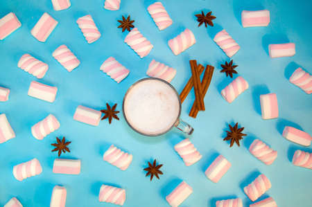 Hot Christmas Drink Cocoa Coffee or Chocolate with Milk and Marshmallows Cinnamon Stick Star Anise and Pieces Chocolate Small Transparent Cup on a Blue Background Winter New Year Flat Lay Top Viewの写真素材