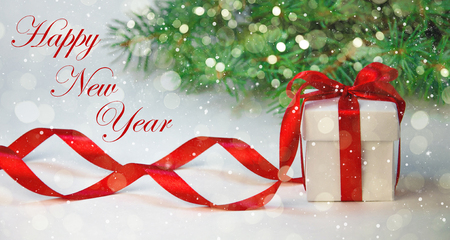 Christmas Gift in White Box with Red Ribbon on Light Background with Fir Tree. New Year Holiday Composition. の写真素材