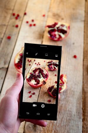 Food Photography on Mobile Phone. Woman Makes Photo Pomegranate on Smartphone.の写真素材