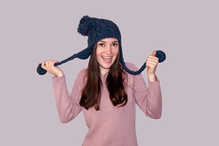 Young Beautiful Woman in Sweater and Funny Knitted Hat on Grey Background. Winter Concept