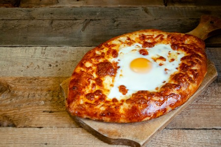 Traditional Georgian Dish. Adjarian Khachapuri with Suluguni Cheese and Egg on Rustic Wooden Table on Dark Background.の写真素材