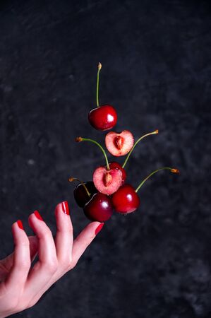 Close up Composition of Levitation Cherries on Woman Finger on the Dark Backgroundの写真素材