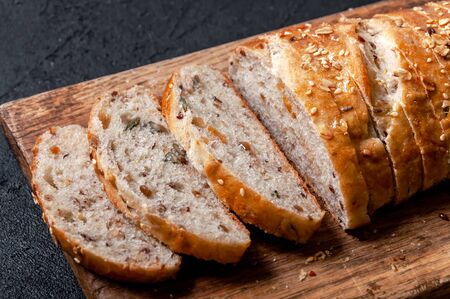 Homemade Sliced Wholemeal Multigrain Bread with Flax Seeds and Sesame on Wooden Board on Dark Table
