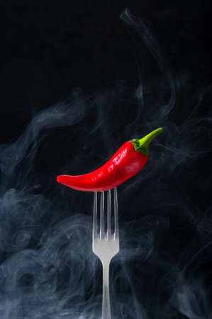 Red Hot Chili Pepper on Fork with Smoke on Black Background.の写真素材