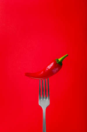 Red Hot Chili Pepper on Fork with Smoke on Red Background.