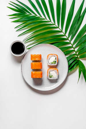 Philadelphia rolls with salmon fish, cucumber and cheese on plate with soy sauce and palm leaf on white background. Top view Flat lay. Minimal concept.の写真素材