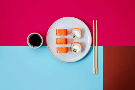 Philadelphia rolls with salmon fish, cucumber and cheese on plate with soy sauce on colorful background. Minimal conceptの写真素材