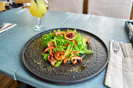 Fresh mediterranean salad with shrimps, octopus, and squid on a black plate on the veranda of the...