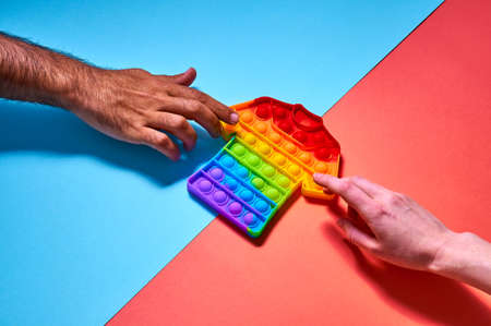 Woman and man hands reaches out to colorful trendy pop toy in form t-shirt on blue background.