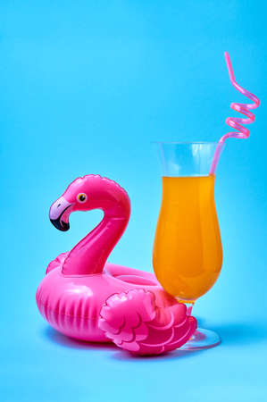 Cocktail tequila sunrise with inflatable pink flamingo pool toy on blue background. Creative summer concept.の写真素材