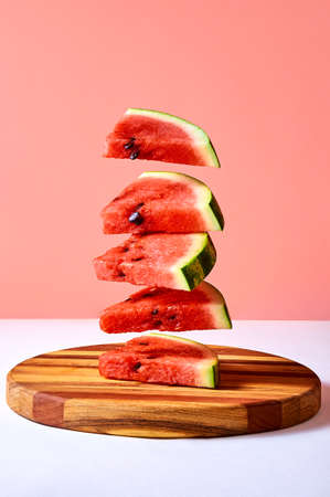 Fresh ripe pieces watermelon flying over wooden board on pink background. Creative minimal conceptの写真素材