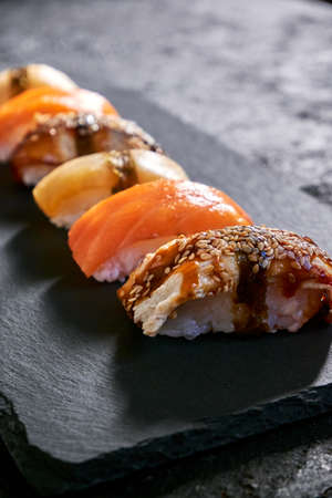 Assorted sushi with salmon, eel and escolar on black stone plate on dark background. Minimal conceptの写真素材