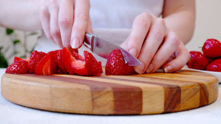 Woman cutting strawberrys on wooden board and preparing smoothie or milkshakeの写真素材