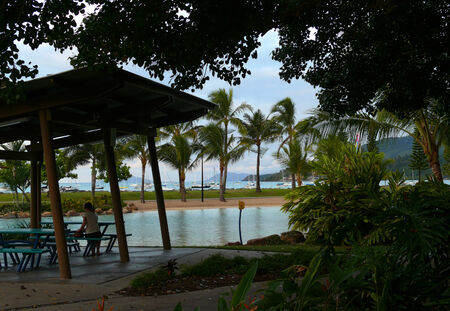 TOWNSWILLE, QUEENSLAND AUSTRALIA - NOVEMBER 8, 2007: Tropical beach with docked sailboats in Townswille, Queensland Australia - 8 November 2007. Girl sitting on a bench under a canopy.のeditorial素材