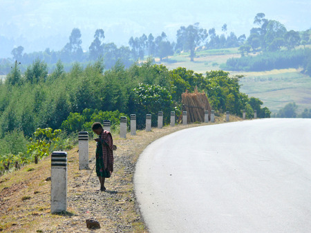 DEMBECHA, ETHIOPIA - NOVEMBER 24, 2008: Unfamiliar Ethiopian child standing on the road in Dembecha, Ethiopia - November 24, 2008. Lonely road. Landscape nature around.のeditorial素材