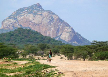 ISIOLO, KENYA - NOVEMBER 28, 2008: A strange man from the tribe Tsonga in national dress goes on the road with a dog in Isiolo, Kenya - November 28, 2008. Mountains in the background. Around the plants and trees.のeditorial素材