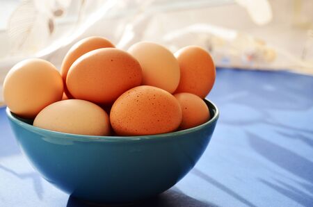 blue plate full of fresh chicken eggs on against the window bright sun shadow from the curtainの写真素材