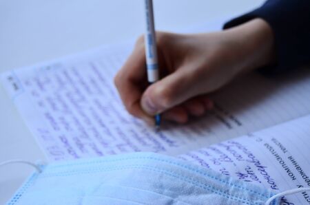 child writes in notebook next to lies medical mask in quarantine horizontal orientation