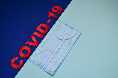 inscription in red letters on a blue background and a medical mask on a mint background with a copy...