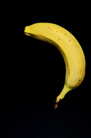 one yellow banana on a black background upside down with copy space vertical orientation horizontal orientationの写真素材