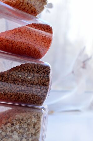 jars of cereal lentil buckwheat oatmeal lined on top of each other against the background of the window view from the sideの写真素材