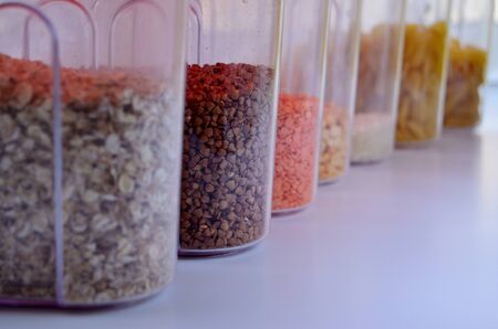 Cans of oatmeal buckwheat lentil peas rice pasta stand in a row against the background of the window sill window sill close-upの写真素材