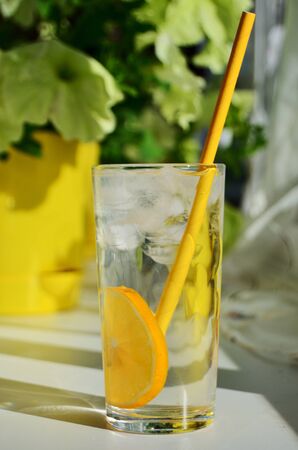 glass glass with water lemon ice and yellow tube on a solar window with flowersの写真素材