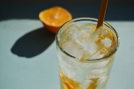 lemon refreshing water with ice in a glass glass with a yellow tube against the background of half a...