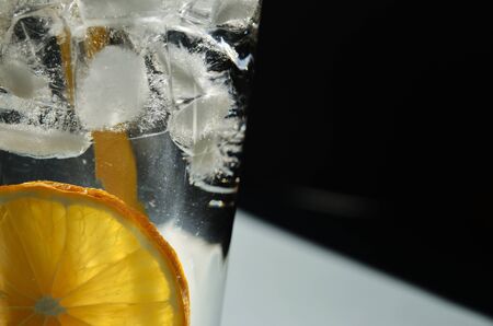 lemon water with ice in a glass glass with a yellow tube close-up on a black background with a copy...