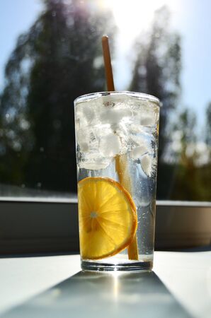 glass glass with water lemon ice and yellow tube against the background of the window with a bright sun view from belowの写真素材