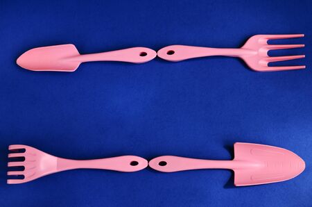 Garden equipment pink shoulder blades and rakes on a blue background are lined in two rows as a frame to copy spaceの写真素材