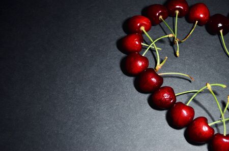 half heart of ripe red cherries on a black background with a copy space for menu and cookbooks horizontal orientationの写真素材