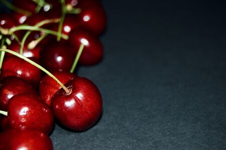 red sweet ripe cherry close-up on the left edge on a black background with a copy space for menu and...