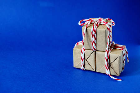 three gifts like a Christmas tree in craft paper tied with a red white rope on a blue background...