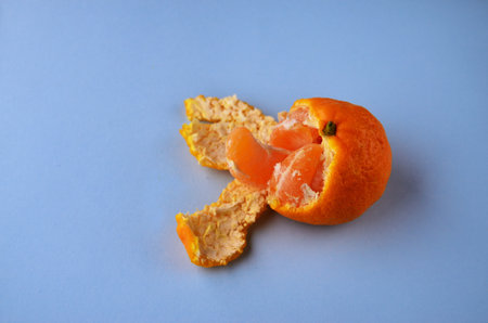 One half peeled tangerine with peel and a slice of tangerine on a blue background with a copy spaceの写真素材