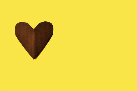 One heart carved from brown cardboard on a yellow background with a copy spaceの写真素材