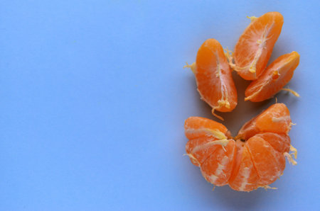 One fresh peeled tangerine with three slices on a blue-colored table view from above with a copy spaceの写真素材