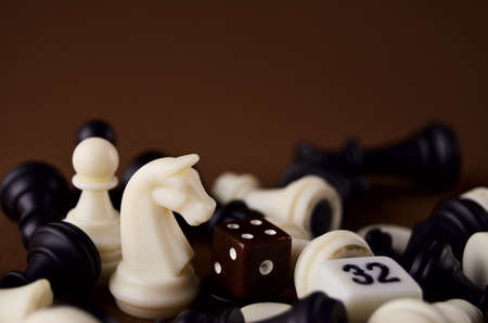 Chess horse figures close up around other chess pieces and dice on a brown background