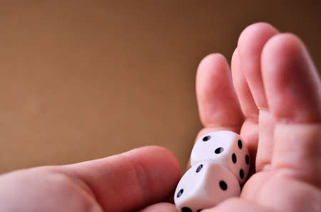 White dice lie in the palm of your hand close up on a brown background with a copy space