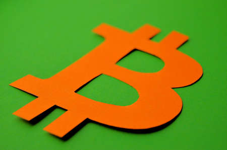 The bitcoin sign carved from orange paper lies on a green background close-upの写真素材