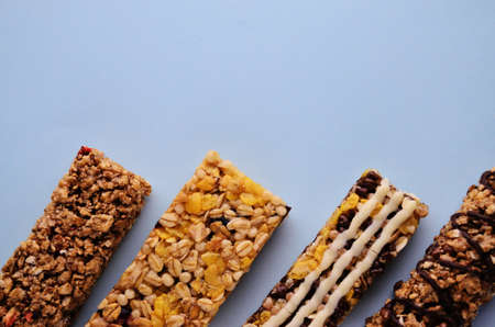 Four bars of granola lie in a row on the lower edge of the photo on a blue background with a copy spaceの写真素材