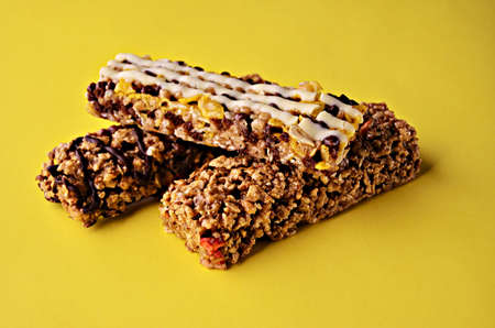 Three bars of granola are stacked on top of each other in the center of the frame on a yellow...